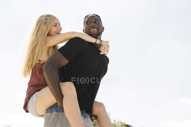 Giovane uomo dando fidanzata un maialino indietro contro cielo blu — Foto stock