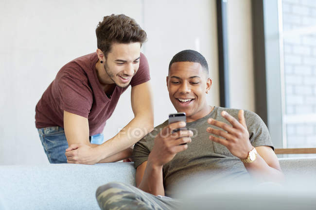 Deux jeunes étudiants masculins dans l'espace d'étude partageant des messages texte au collège d'enseignement supérieur — Photo de stock