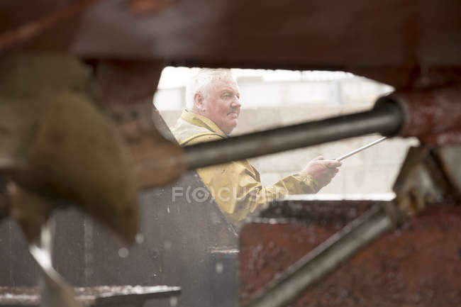 Pintor de barcos macho senior limpiando casco de barco con arandela a presión en astillero de pintores - foto de stock