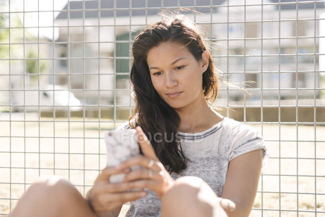 Femme lisant les mises à jour du smartphone par clôture métallique — Photo de stock