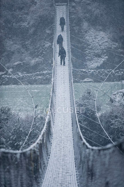 People crossing snowy rope bridge — Stock Photo