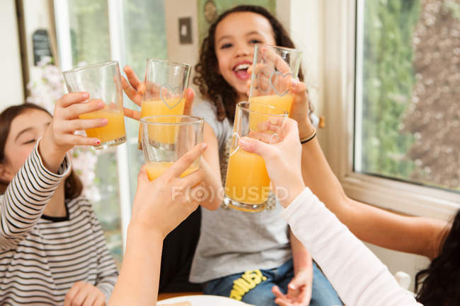 Filles faire des toasts avec des verres de jus de fruits à la table à la maison — Photo de stock