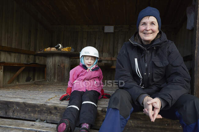 Fille portant un casque de ski assis sur le pas de la grange avec grand-mère, Gavle, Suède — Photo de stock