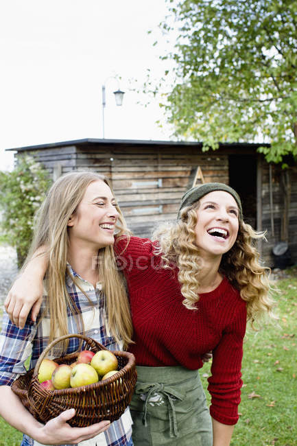 Due donne in giardino con cesto di mele, ridendo — Foto stock