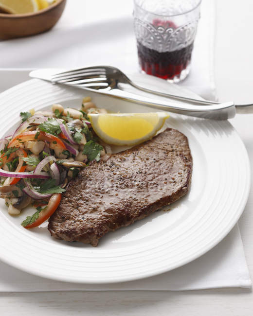 Steak avec oignon rouge, haricots blancs, tomates, persil et tranche de citron — Photo de stock