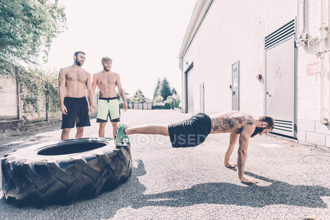 Junger männlicher Crosstrainer macht Liegestütze aus Reifen außerhalb des Fitnessstudios — Stockfoto