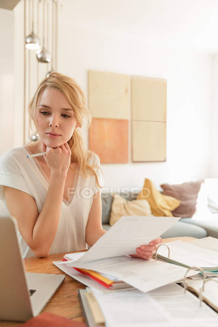 Frau arbeitet mit Papierkram und schaut auf Laptop — Stockfoto
