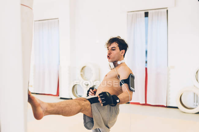 Homem no ginásio usando monitor de frequência cardíaca chutando saco de soco — Fotografia de Stock