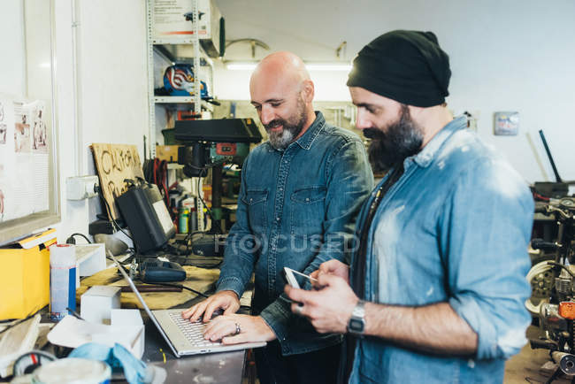 Deux hommes mûrs, travaillant dans un garage, utilisant un ordinateur portable — Photo de stock