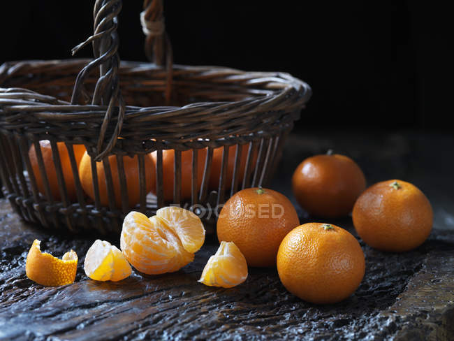 Frische ganze und geschälte Mandarinen neben Korb — Stockfoto