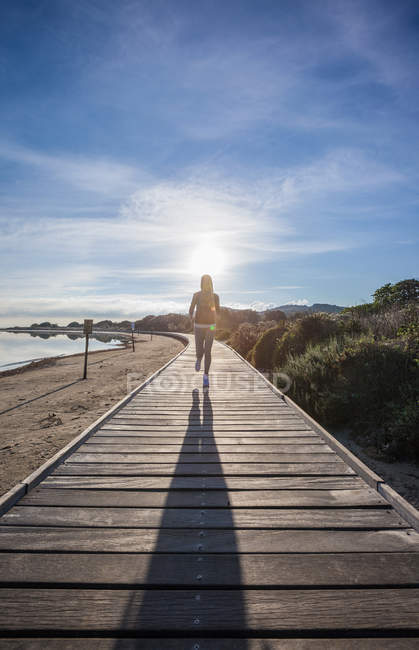 Female runner and her shadow running along beach boardwalk, Villasimius, Sardinia, Italy — Stock Photo