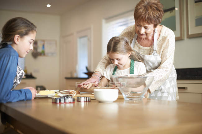 Seniorin und Enkelinnen rollen Teig für Christbaumkuchen — Stockfoto