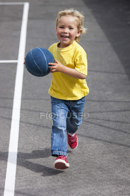 Дошкольник бегает с мячом во дворе — стоковое фото