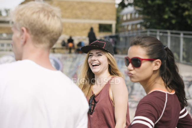 Tres amigas y amigas riendo en el parque de skate de la ciudad - foto de stock