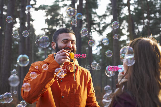 Pareja joven soplando burbujas en el bosque - foto de stock