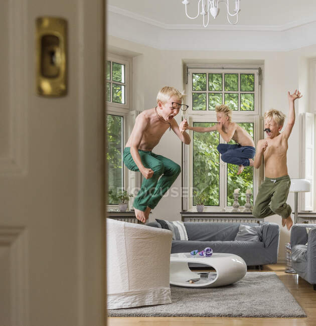 Boys in living room jumping in mid air — Stock Photo