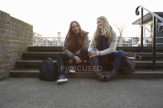 Two female friends sitting on steps and smiling — Stock Photo
