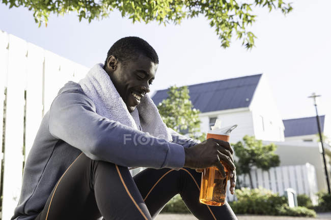 Man in residential area sitting on kerb holding water bottle looking down smiling — Stock Photo