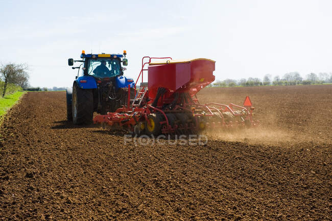Farm tractor and seed drill sowing ploughed field in spring — Stock Photo