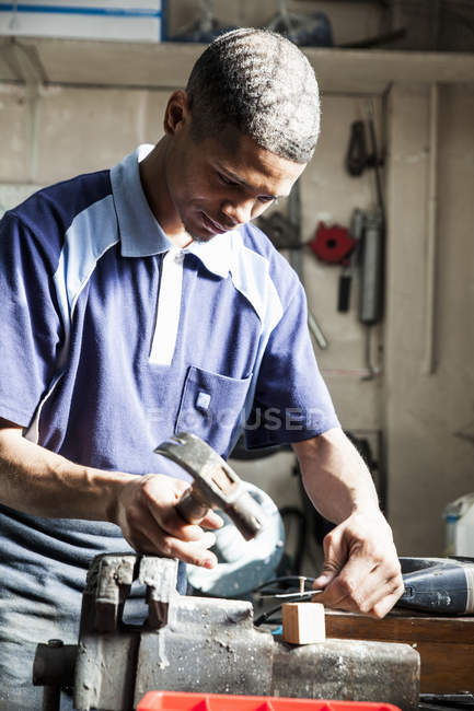 Young man hammering nail in repair workshop — Stock Photo