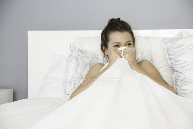 Jeune femme assise dans son lit se cachant — Photo de stock