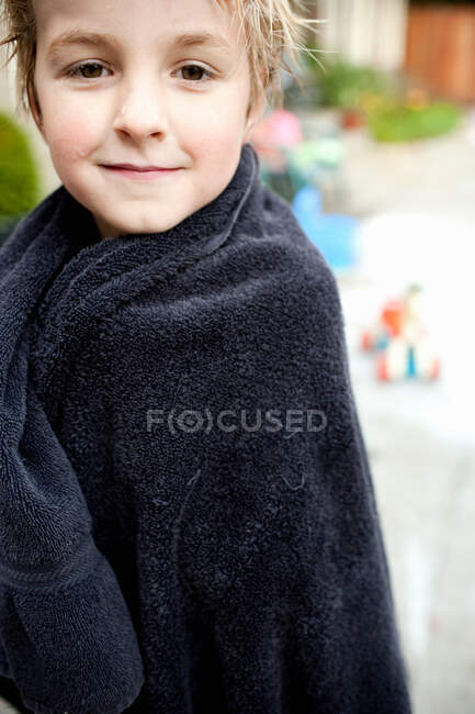 Jeune garçon enveloppé dans une serviette regardant la caméra — Photo de stock