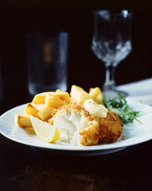 Хлебная рыба с чипсами, ракетой и ломтиком лимона на белой тарелке — стоковое фото