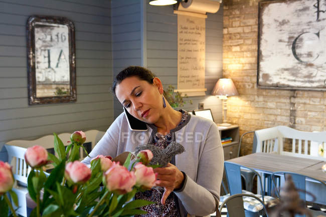 Menú de lectura de cliente femenino maduro mientras habla en el teléfono inteligente en la cafetería - foto de stock