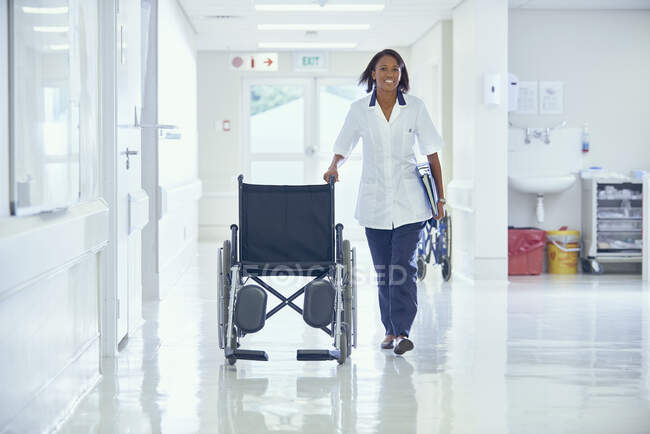 Femmina ordinata spingendo sedia a rotelle lungo il corridoio dell'ospedale — Foto stock