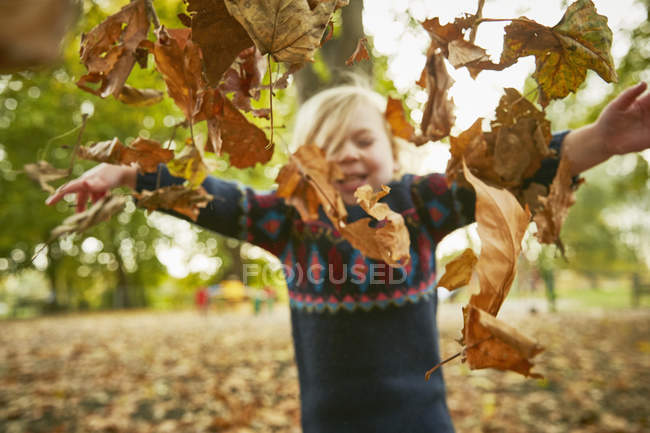 Дівчинка кидає в осіннє листя — стокове фото