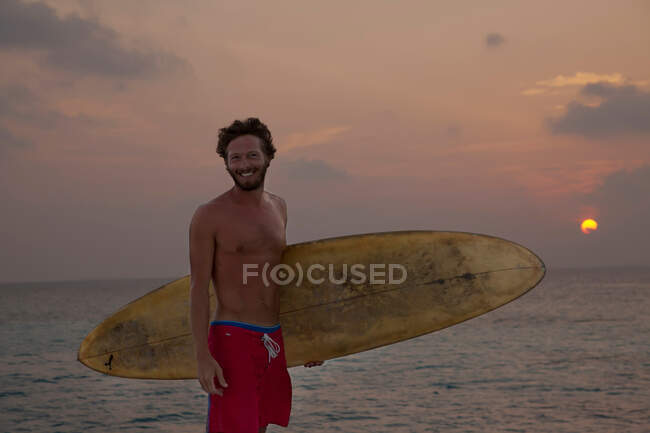 Surfer carrying board on beach at sunset — Stock Photo
