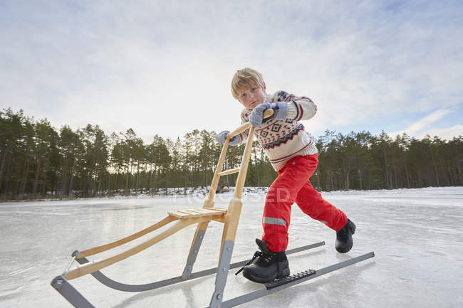 Niño empujando kicksled a través de lago congelado, Gavle, Suecia - foto de stock