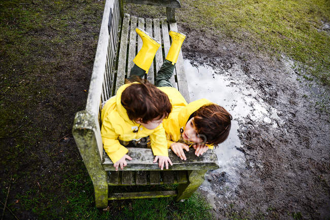 Vista aérea del bebé y el hermano en anoraks amarillos en el banco del parque - foto de stock