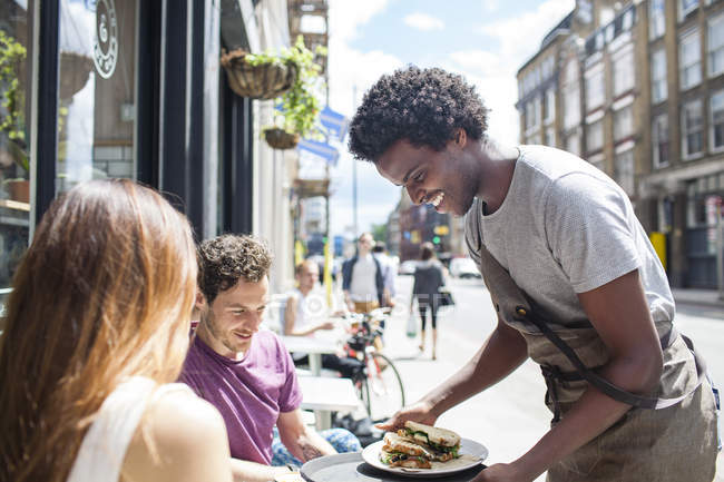 Waiter serving lunch to couple at city sidewalk cafe — Stock Photo