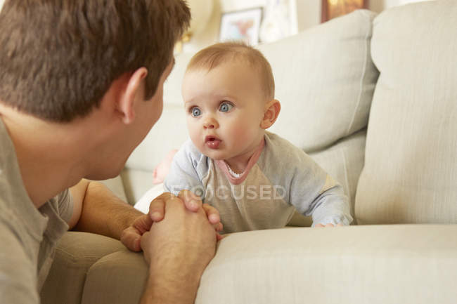 Cute blue eyed baby girl on sofa staring at her father — Stock Photo