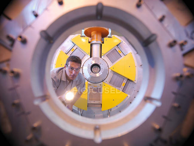 Male scientist inspects particle accelerator with a torch — Stock Photo