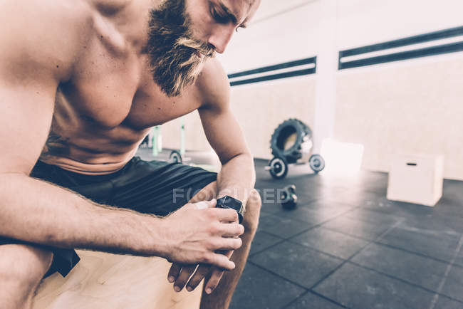 Jeune homme assis vérifier smartwatch dans la salle de gym cross-training — Photo de stock