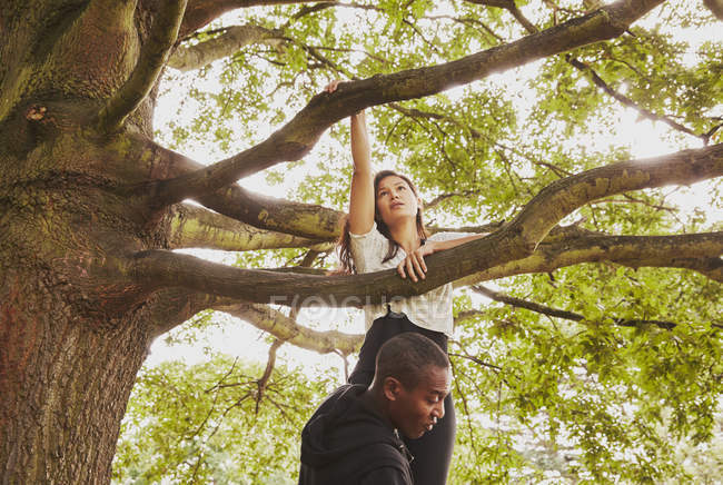 Personal trainer lifting woman to climb park tree — Stock Photo