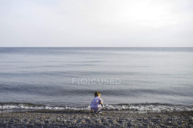 Vista posteriore del piccolo ragazzo accovacciato e che gioca al lago Ontario, Oshawa, Canada — Foto stock