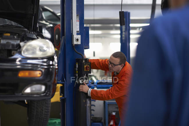 College mechanic student operating car lift in repair garage — Stock Photo