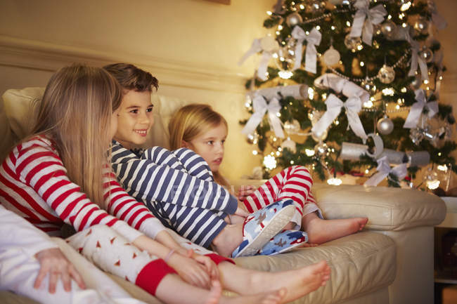 Ragazzo e ragazze in pigiama a righe sul divano a Natale — Foto stock