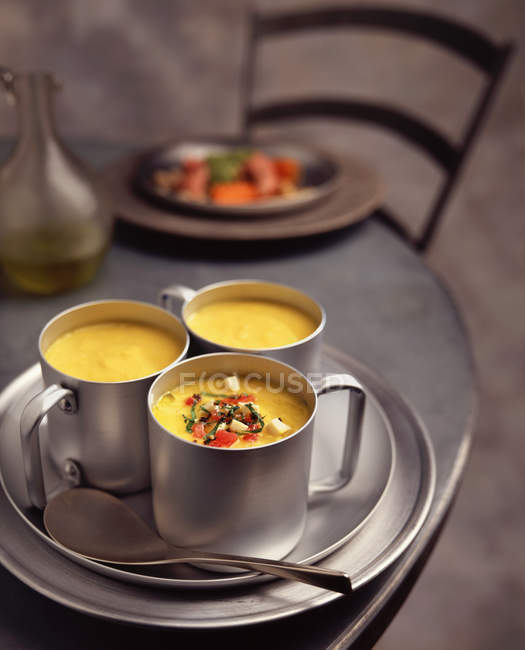 Жовтий перець суп з помідорами, сиром фета та трав'яним гарніром у металевих чашках — стокове фото