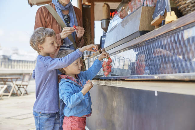 Madre e hijos caucásicos comprando caramelos, Londres, Reino Unido - foto de stock