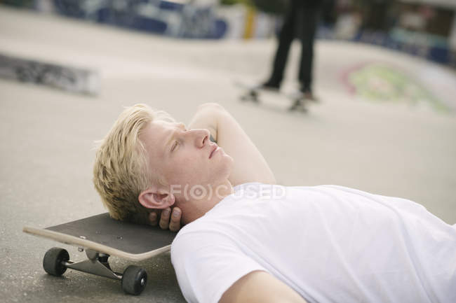 Молодий чоловік скейтбордист лежить в скейтпарку з закритими очима — стокове фото