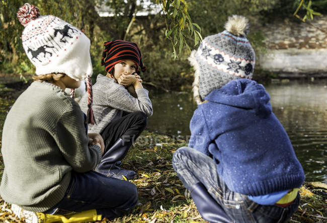 Three young boys, outdoors, crouching beside lake — Stock Photo