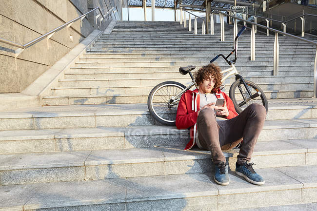 Man sitting on steps with BMX and using smartphone — Stock Photo