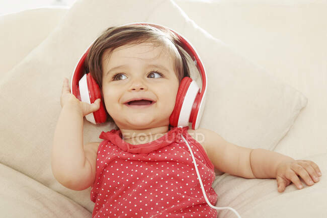 Menina no sofá ouvindo fones de ouvido vermelhos — Fotografia de Stock