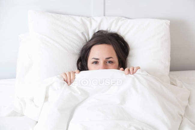 Femme se cachant sous les couvertures au lit — Photo de stock