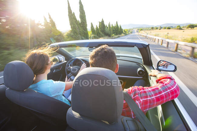Rear view of couple driving convertible on sunlit rural road, Majorca, Spain — Stock Photo