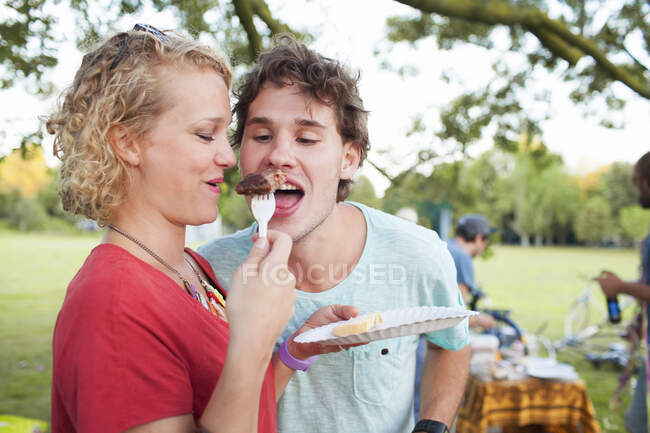Jovem feliz e mulher compartilhando comida na festa do pôr do sol no parque — Fotografia de Stock